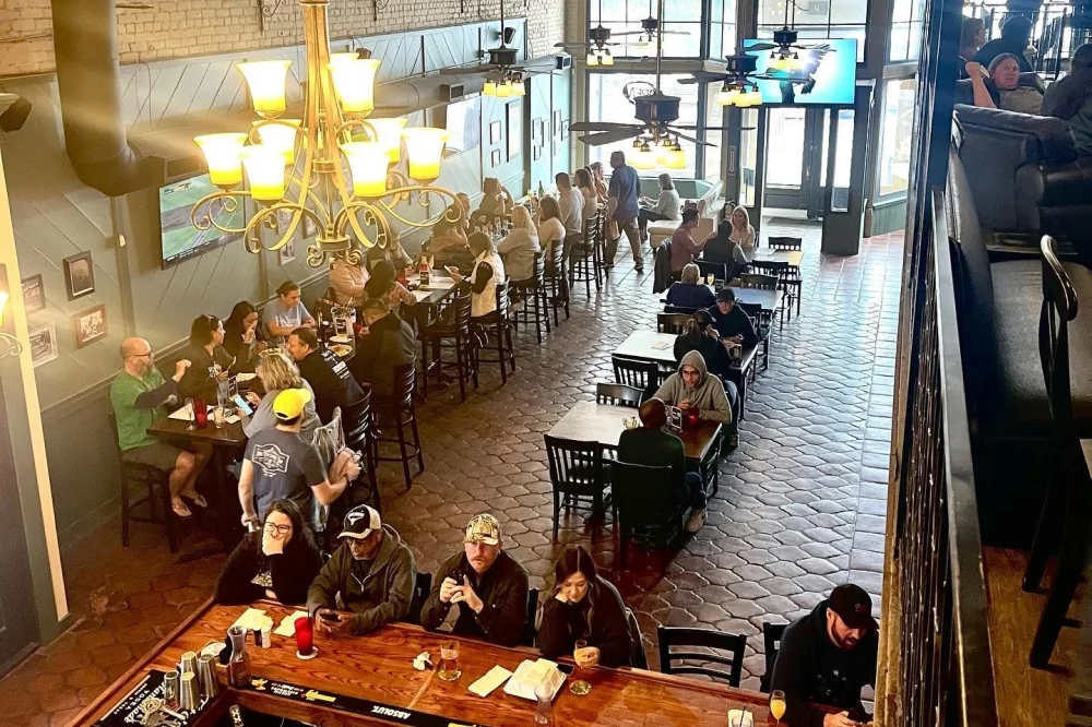 The Victory Tap’s historic dining room, tall windows and chandeliers, seen from the mezzanine.