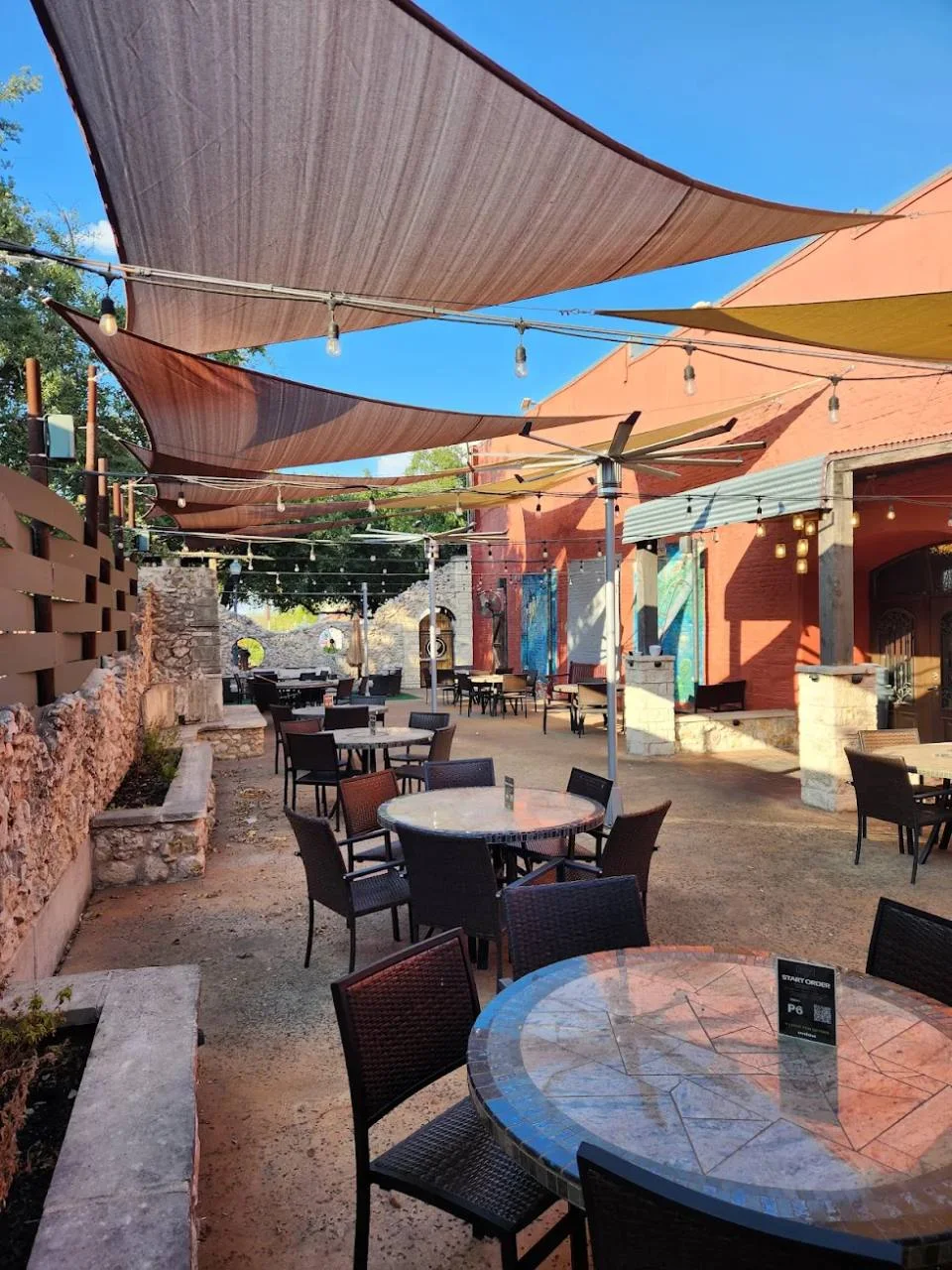The Victory Tap patio — sun sails, string lights, stone walls and tables set for the afternoon