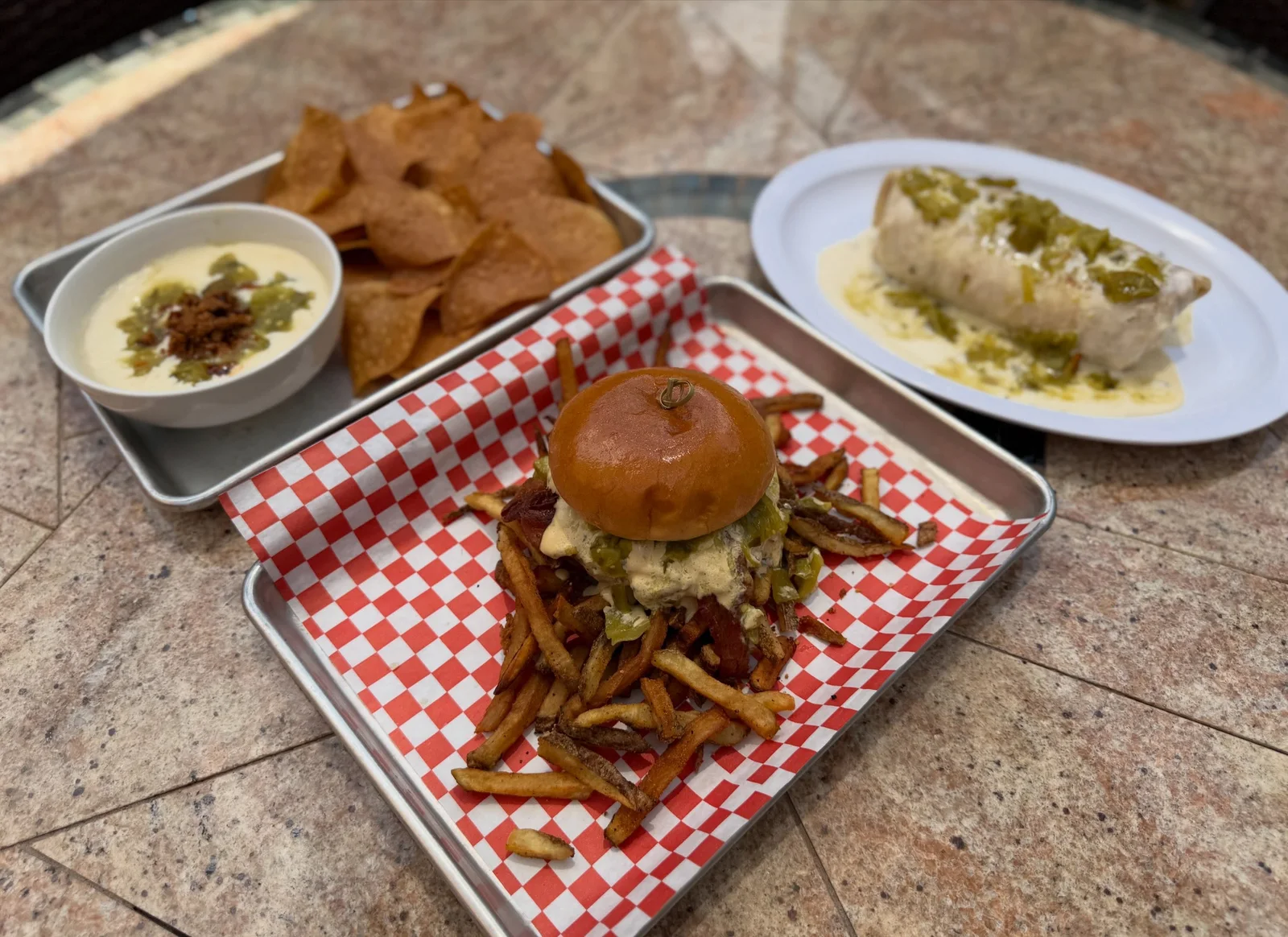 A full Victory Tap spread with a burger, fries, chips, queso and a seasonal entrée on a mosaic table.